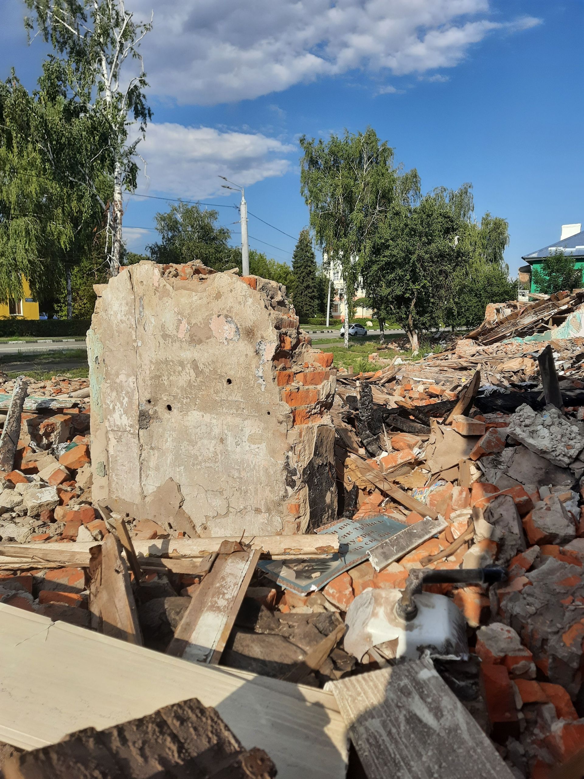 A pile of rubble and broken bricks under a clear blue sky, surrounded by trees.