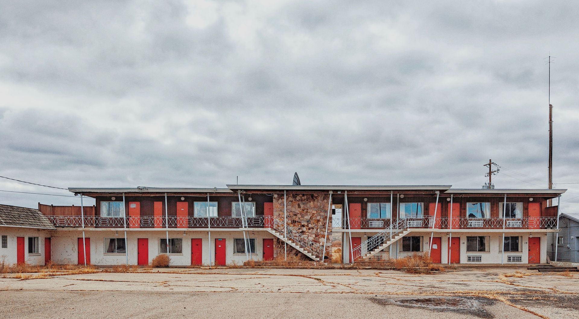 A deserted mid-century motel with a cloudy sky, featuring red doors and an empty parking lot. United States.