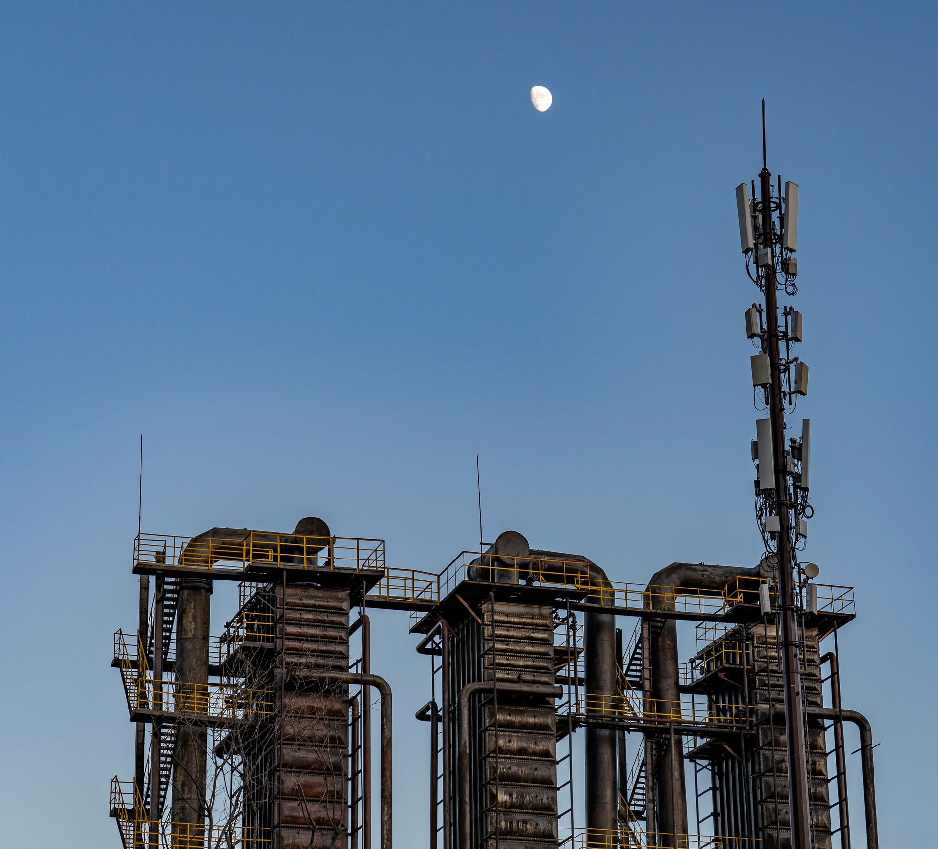 Low angle view of an industrial factory against a clear blue sky with the moon visible.